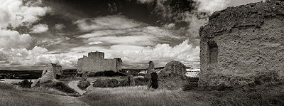 The grassy outer bailey of Château Gaillard; the land slopes away to a ditch, separating the outer bailey from the middle bailey. Parts of the wall surrounding the middle bailey still stand. To the right is part of the wall of the outer bailey. In the background the keep rises above the walls of the inner bailey.