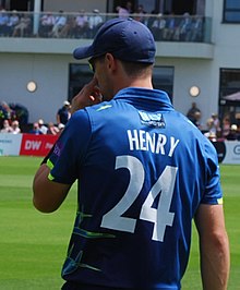 A head and shoulders photograph taken from behind of a cricketer fielding whilst wearing a blue uniform with the number 24 on his back