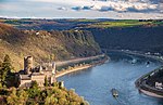 A river winds between high cliffs and hills, with a castle in the midground.