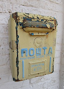 A yellow postbox with POSHTA written on it in blue and in the Cyrillic script.