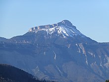 Montagne enneigée dominant une barre rocheuse en avant-plan.