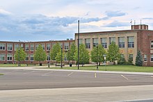 A high school with blue sky above and parking lot in foreground