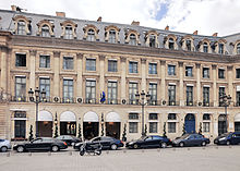 Photographie en couleur d'une bâtiment, vu légèrement de profil, de style classique à quatre niveaux. La façade présente sur la hauteur du rez-de-chaussée et de l'entresol des chaînes de refends et se caractérise également par une alternance de lucarnes et oculi.