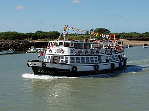 A small white ferry carrying passengers in the mouth of the Guadalete river