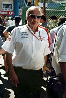 Photo d'un homme debout, en chemise blanche et portant des lunettes de soleil