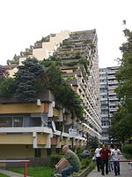 Blok mieszkalny z widokiem na Alpy, „Pharao-Haus” („Pyramide”) w Monachium w Niemczech Zachodnich, architekt Karl Helmut Bayer, 1974. Tarasowiec (niem. Terrassenhochhaus) reprezentuje późny modernizm i zaliczany jest do brutalizmu. Architektura humanistyczna, a nie masowa. Nowatorski blok mieszkalny będący rezultatem wyciągnięcia wniosków z błędów dotychczasowej architektury mieszkaniowej modernizmu w tym brutalizmu. Modernistyczna architektura w tym przypadku dzięki nowatorstwu swoich rozwiązań takich jak duży metraż przypadający na każdą osobę i całkowite przeszklenia mieszkań zamiast małych okien zapewnia wyższy poziom życia niż w powojennych blokach mieszkalnych zarówno biednego Wschodu, jak i bogatego Zachodu. Prywatne tarasy przylegające do różnorodnych mieszkań są pełne zieleni i same mają imponującą powierzchnię małych mieszkań. Dodatkową innowacją jest brak negatywnej ingerencji w krajobraz przez żelazobetonowy budynek, który sam wnosi więcej roślinności do otoczenia niż ukwiecony dom jednorodzinny[15].