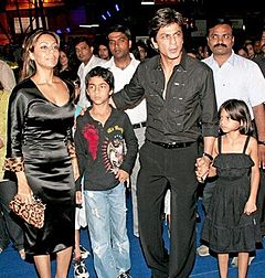 Shahrukh Khan debout, avec un enfant de chaque côté de lui, et une femme.