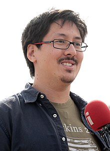 Ronald Watkins pictured from the shoulders up, wearing a brown-green t-shirt and glasses.