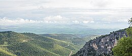 Colour photograph of foothills descending into a plain, with clouds in the distance