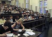 Les étudiants écoutent le professeur, certains prennent des notes.