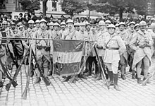 Soldats autour d'un drapeau tricolore. La hampe du drapeau est posée horizontalement sur deux trépieds de fusils.