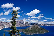 Wizard Island is shown in Crater Lake, with clouds in the sky above. The caldera rim appears to the left.