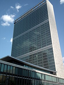 View of the building from the southwest, with the Dag Hammarskjöld Library in the foreground. The western facade at left is made of glass, while the southern facade at right is clad in stone.