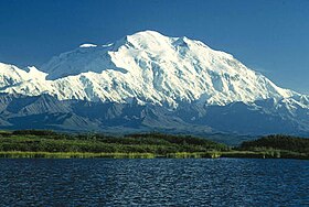 A snow-covered, gently sloping mountain is in the background, with a lake in the foreground