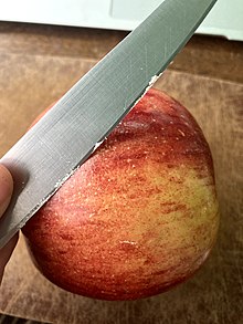 Person shaving synthetic wax from a red apple with a knife.