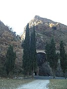 Chemin plat menant à une haie d'arbres, puis derrière un pont et des falaises.