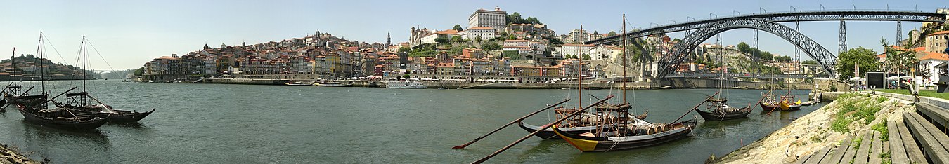 Panorama miasta od strony Vila Nova de Gaia, miasta po przeciwnej stronie rzeki Duero. Na pierwszym planie barki, którymi spławiano tradycyjnie wino z plantacji. Po prawej charakterystyczny most Ponte Dom Luís I z 1886 roku, projektu ucznia Gustawa Eiffla. Na wprost historyczna dzielnica Ribeira.