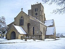 Stone building with gravestones in foreground and to the left; the church tower is surmounted by an ornamental weathercock, and has a clock showing 10.35. The roofs and surrounding areas are covered in snow.