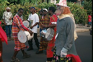 Band members performing on drums while in the street; one member is wearing a monkey mask and comic hat.