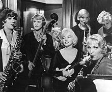 Monroe tocando el ukelele con un travestido Lemon en el bajo y Curtis en el saxofón. También hay otras tres mujeres tocando instrumentos diferentes.