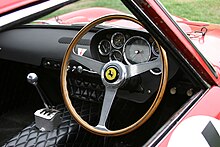 Looking through open driver's window of a right-hand-drive car, showing brown steering wheel with three metal spokes, gear lever and dashboard