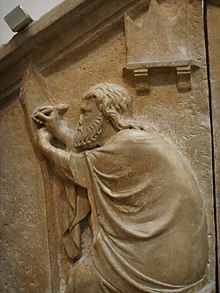 Relief ob steni prikazuje bradatega moškega, ki sega z rokami, oblečena po telesu.