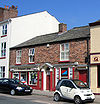 A brick building in two storeys with modern shop fronts and a pedimented doorway