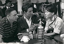 Photo en noir et blanc de deux hommes et une femme discutant à la terrasse d'un café.