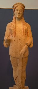 Kore nº 670, del 500 a. C., con la expresión facial típica del arte arcaico (la «sonrisa arcaica»). En una mano, llevaría las ofrendas (flores, pájaros, fruta).