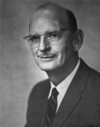 A photographic portrait of a man wearing glasses and a suit