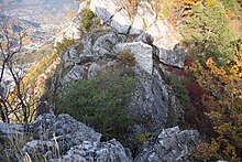 Trou entre deux rochers. Un mur en pierres est construit sur le rocher le plus loin et des buissons se trouvent entre les deux rochers.