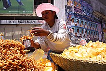 Woman selling chips and fried snacks in baskets on street curb