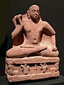 Le Buddha kapardin[9] en dhoti sur le trône aux lions. empire kouchan, fin Ier siècle ou début IIe siècle. Région de Mathura. Grès rose tacheté. Linden-Museum, Stuttgart