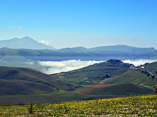 English: Clouds in the valley, mountains and hills in sunshine, blue sky, Castelluccio and small Colle Tamburo in July 2016.