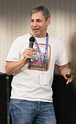 A man wearing a white t-shirt speaking into a handheld microphone