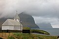 Die Kirche von Viðareiði am westlichen Ufer im Norden von Viðoy. Im Hintergrund sind die Klippen von Kalsoy und Kunoy zu sehen.