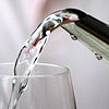 Clear water pours from a spout into a drinking glass.