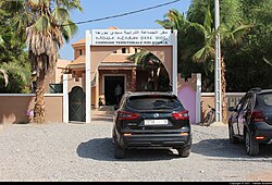 Cars parked outside the Sidi Borja headquarters. There is a sign over the walkway identifying it in multiple languages.