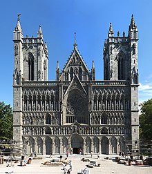 Una iglesia románica con dos arcos apuntados góticos. Dos torres rectangulares separadas por un salón de entrada con techo inclinado. La fachada ornamental está articulada fuertemente con arcos repetivos, la mayoría de ellos enmarcando estatuas.