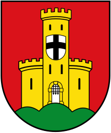 A shield with a red background, an orange castle in ruins, has a second shield of silver with a black cross.