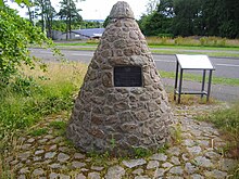 a grassy area with a triangular stone cairn in it