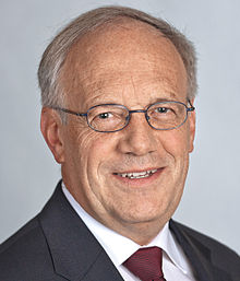 Portrait d'un homme caucasien aux cheveux gris, souriant et portant des lunettes.