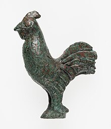 Photographie d'une statuette de coq en bronze, de profil, de couleur marron-vert.
