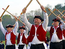 Men in bright red clothing holding sticks in the air.