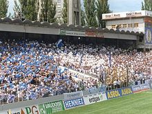 Photographie en couleur d’une tribune d’un stade de football remplie de supporters