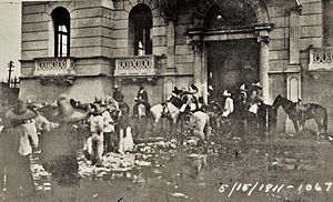 Black and white photograph of a group of men wearing sombreros surrounding a stone building. Dated 5/15/1911.