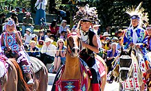 Fotografia a colori di bambini tsuu t'ina in costume tradizionale a cavallo a una Stampede Parade di fronte a un pubblico
