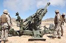 Marines gather around a M777 howitzer, while the smoke from a recently fired round lingers