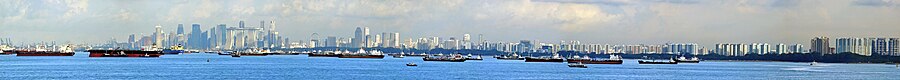 စင်ကာပူ အိစ်ကုတ် ပန်းခြံအလွန် ကျောက်ချရာ နေရာတွင် ကျောက်ချ ရပ်နားထားသော သင်္ဘောများကို စင်ကာပူမြို့ နောက်ခံဖြင့် မြင်ရပုံ