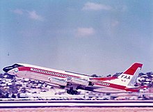 Photo couleur d'un avion aux couleurs blanches, rouges et noires, juste après le décollage, vu du côté gauche.